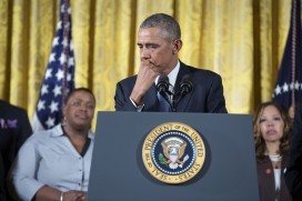 Photo of Barack Obama standing at podium with the presidential seal, pausing with hand to mouth and looking a little bit teary